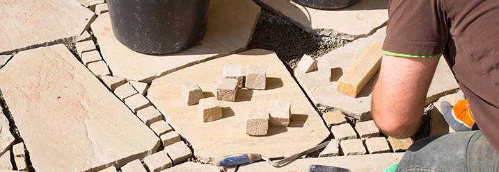 Person verlegt Steinplatten mit Gummihammer